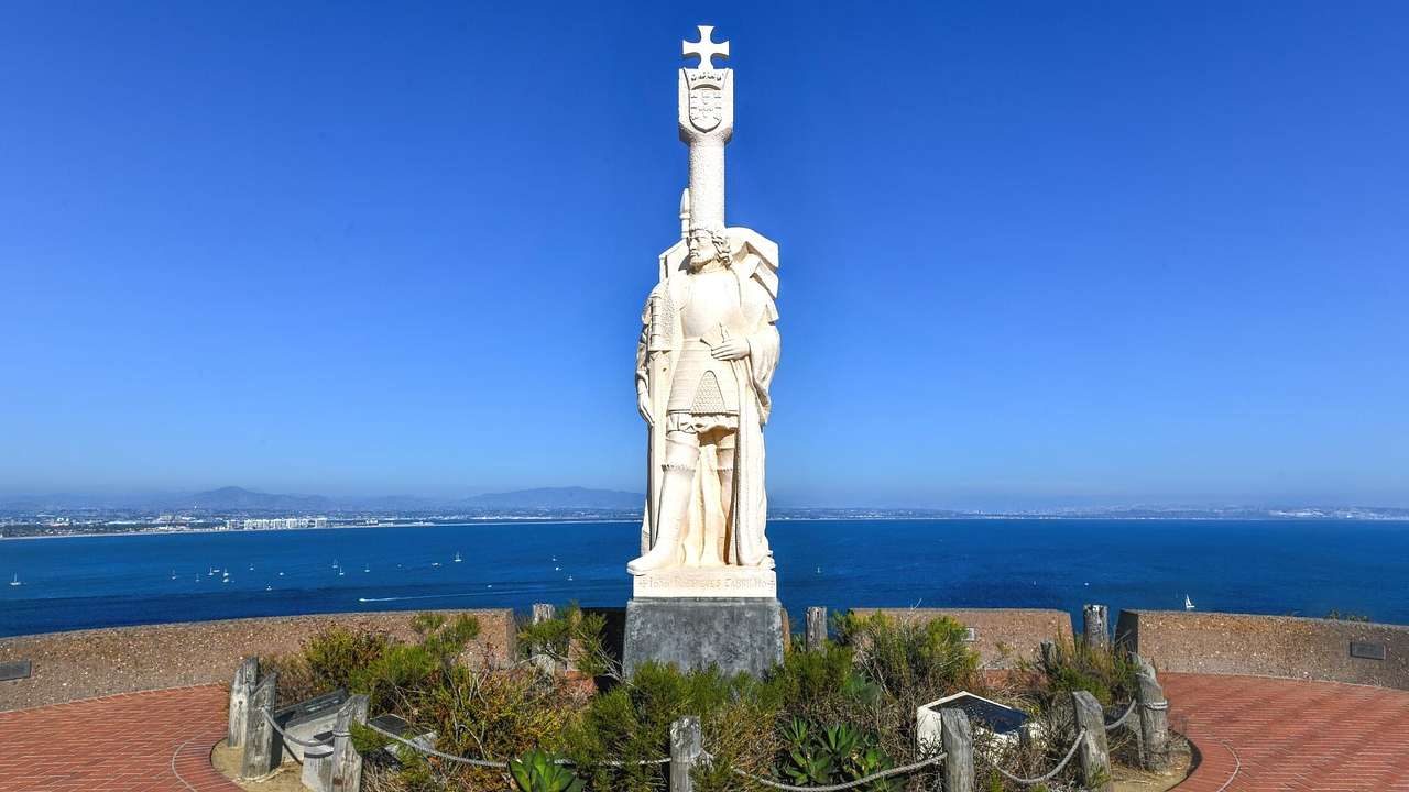 A stone statue of a man with a small garden around it and the ocean behind