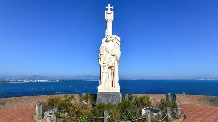 A stone statue of a man with a small garden around it and the ocean behind