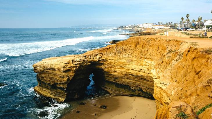 A cliff next to the ocean with palm trees and buildings in the distance