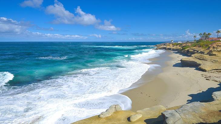 Ocean waves flowing onto a small sandy beach with some palm trees in the distance