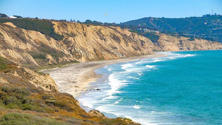 The ocean and a crescent-shaped beach and cliffs with hang gliders in the distance