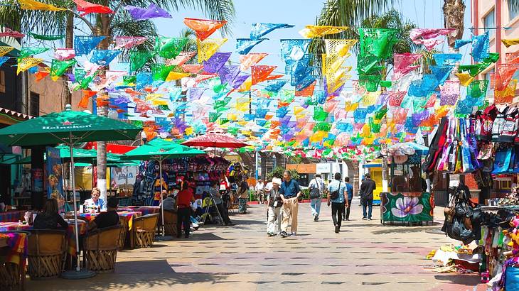 A street with a restaurant with patio umbrellas and colorful flags hanging above