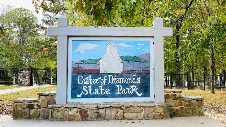 A wooden sign with a picture of a white barn and "Crater of Diamonds State Park"