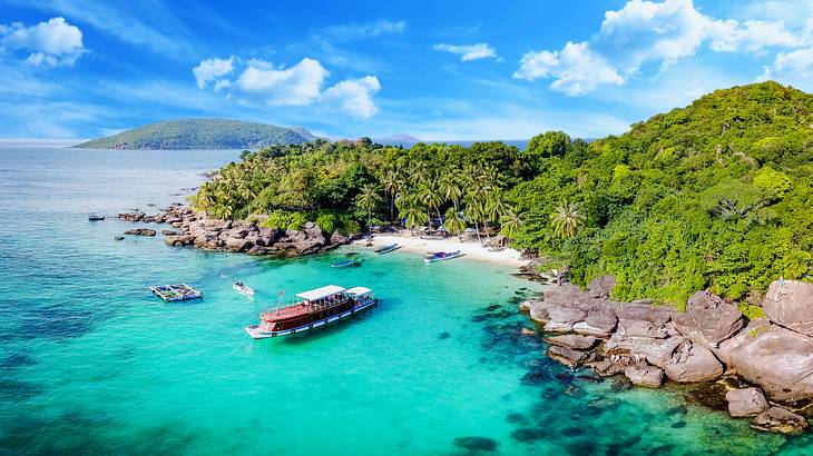 An aerial shot of boats on turquoise water by a beach shore on an island