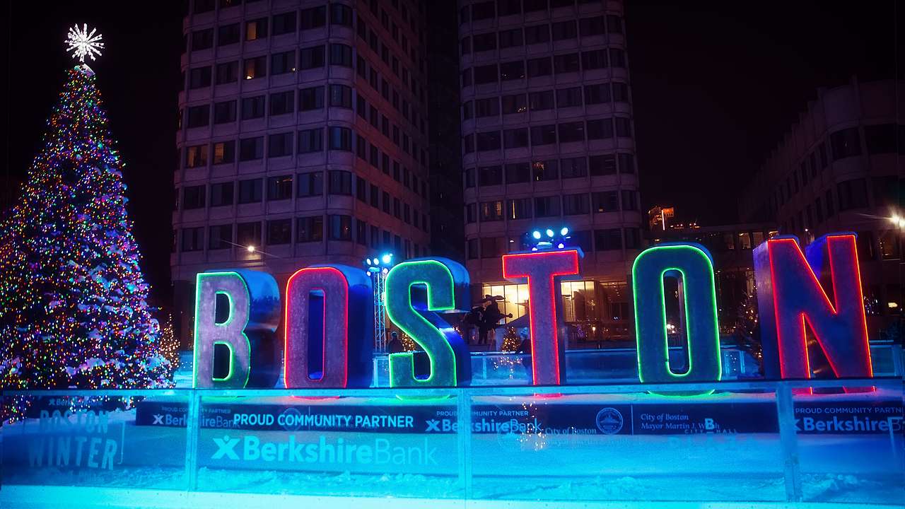 An outdoor skating area at night with neon "Boston" letters and a Christmas tree
