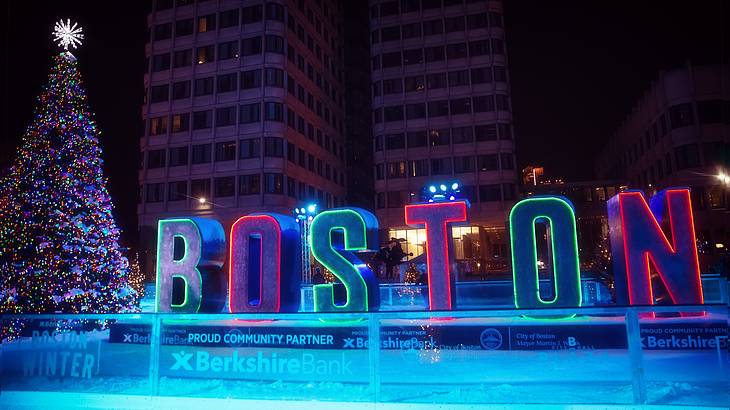 An outdoor skating area at night with neon "Boston" letters and a Christmas tree