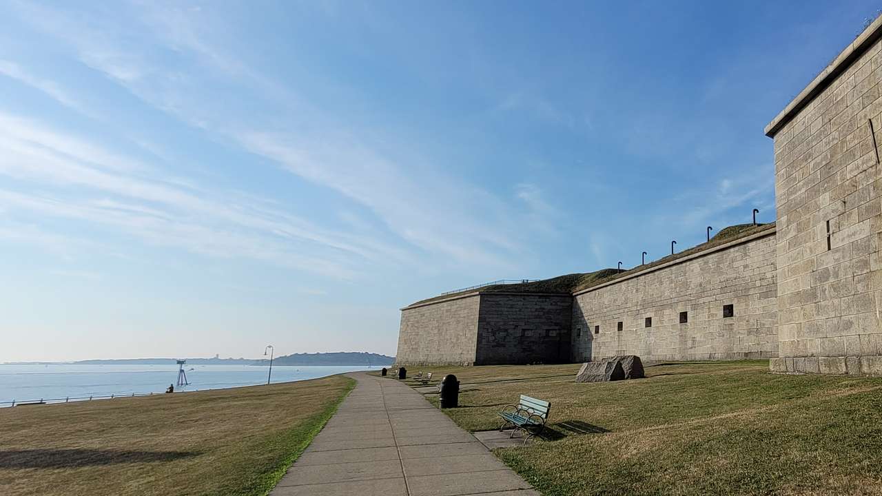 A grey stone building with a walkway and grass by the water