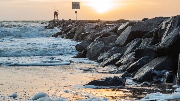 A beach with waves crashing on grey rocks at sunrise