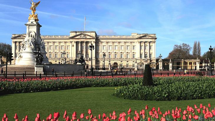 A massive palace with a statue, flowers and grass in front A massive palace with a statue, flowers and grass in front