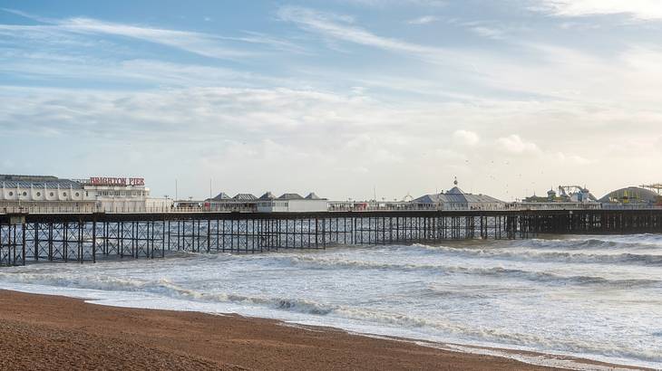 A very long pier above the sea waves with buildings at the back