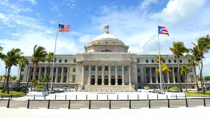 A stone building with columns and trees and US and Puerto Rican flags in front of it