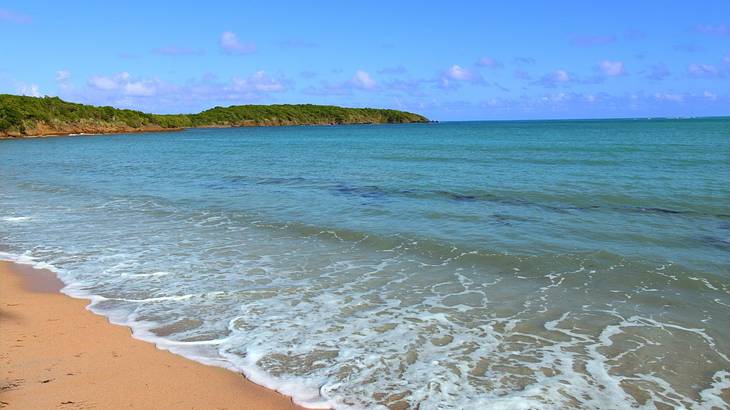 Ocean waves crashing onto the sand with a green island in the distance