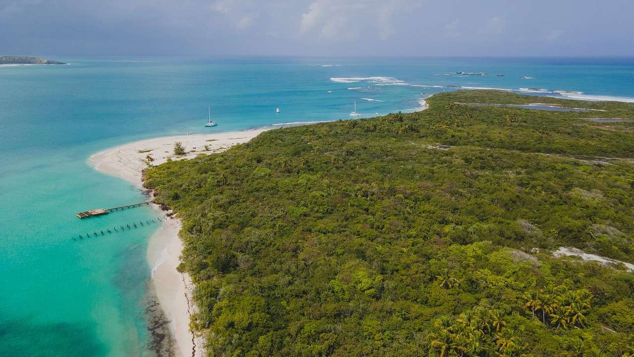 A greenery-covered island with the turquoise ocean and white sand to the side