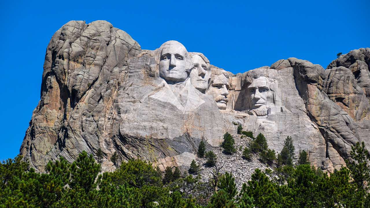 A rocky mountain with the faces of four men carved near the top under a blue sky