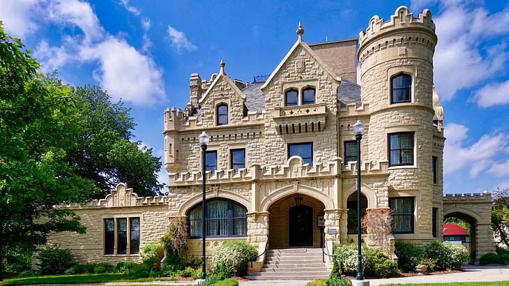 A large stone castle with a walkway surrounded by greenery and lamp posts