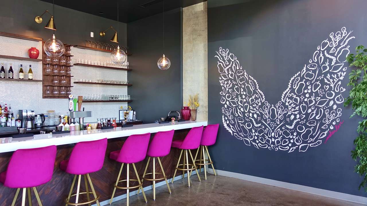 A dining counter with fuchsia chairs and a grey wall with painted white angel wings