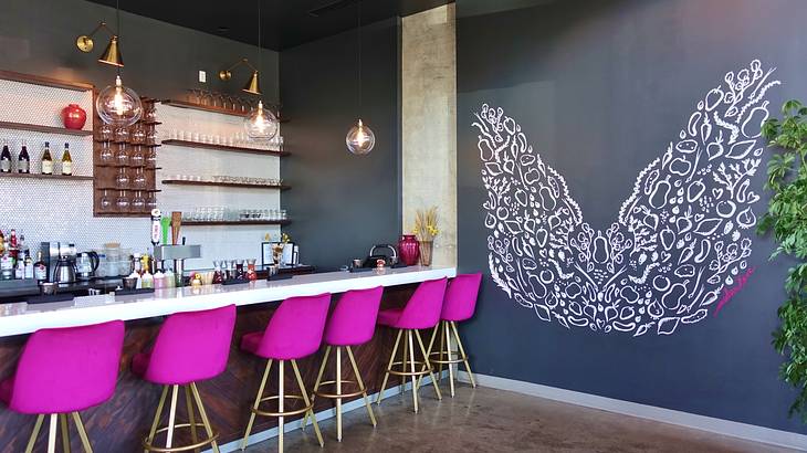 A dining counter with fuchsia chairs and a grey wall with painted white angel wings