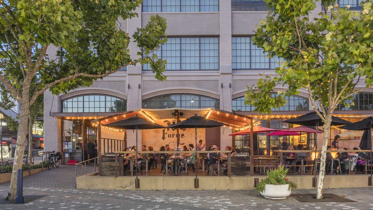 The exterior of a restaurant with patio seating next to a path and trees