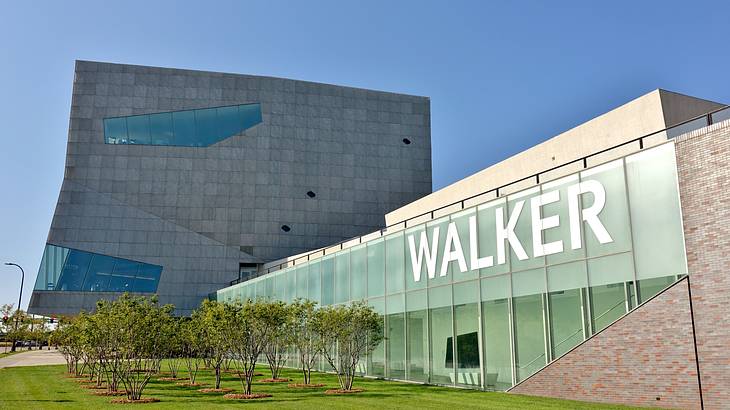 A large building with a glass facade facing a green lawn with tall shrubs