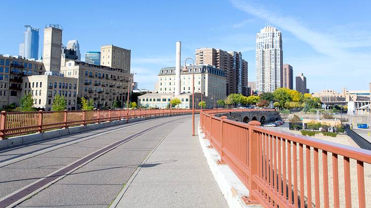 A long brick bridge with red rails going leading to a city with tall buildings