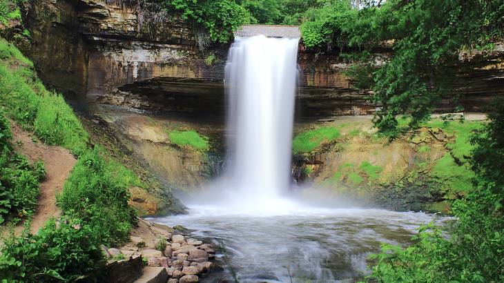 Water gushing from a rocky ledge into a pool of water surrounded by greenery