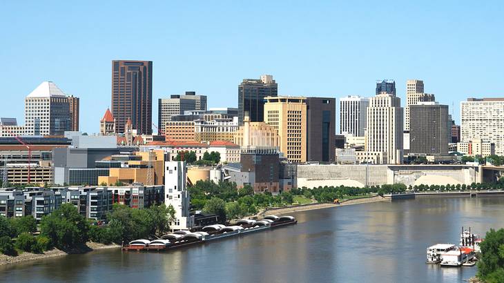 A city skyline with buildings and trees next to a river on a clear day