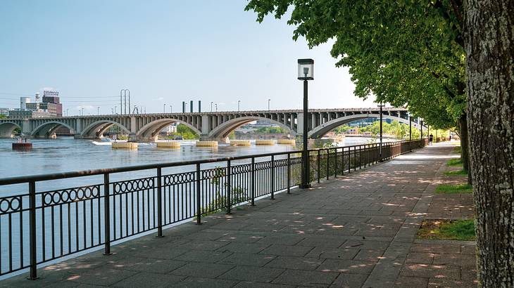 A bricked pathway along a river with a bridge over it