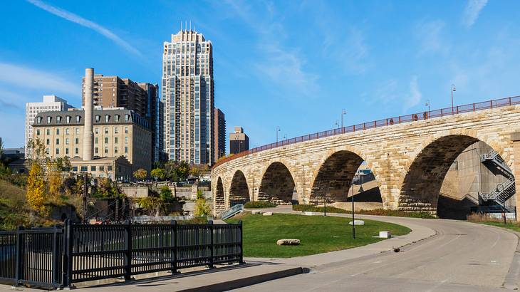 A stone and brick bridge beside a park and buildings