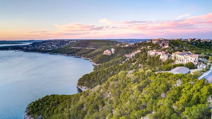 A view over a lake and greenery-covered hills with buildings on them at sunset