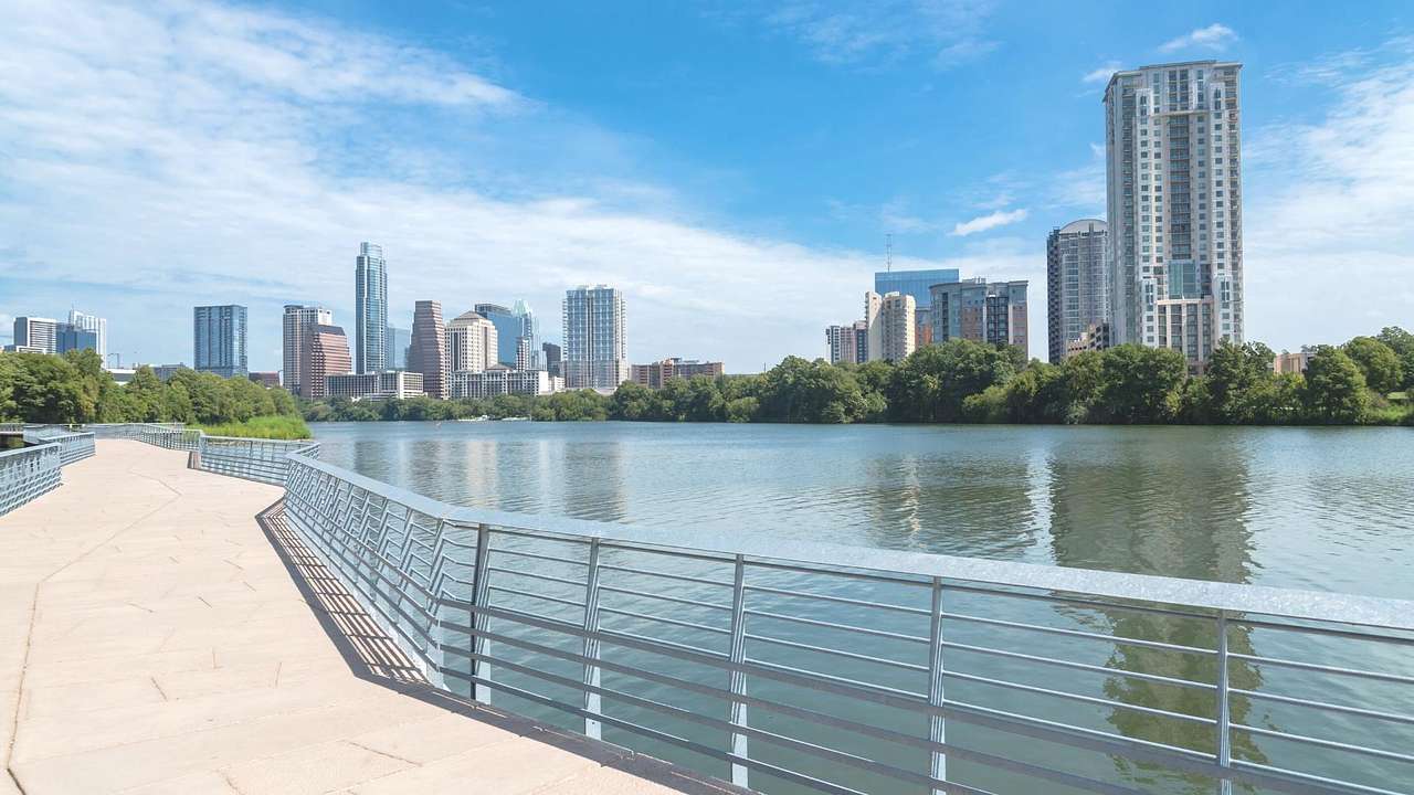 A lake with a boardwalk on one side and a city skyline behind it