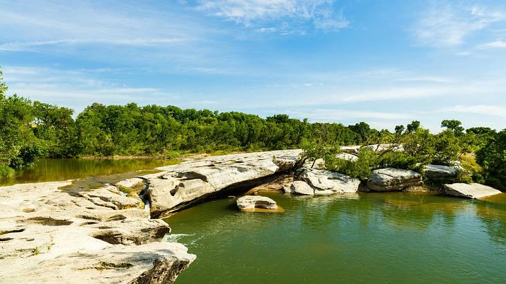 Rocks over a lake with trees on the shore under a blue sky with clouds