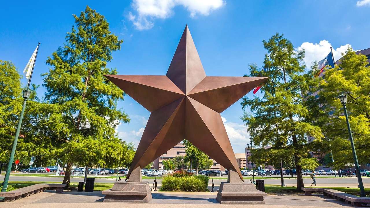 A bronze star sculpture with trees next to it and a parking lot behind it