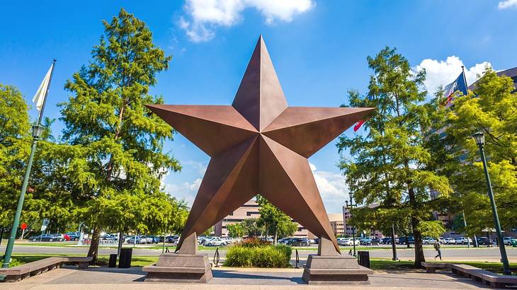 A bronze star sculpture with trees next to it and a parking lot behind it