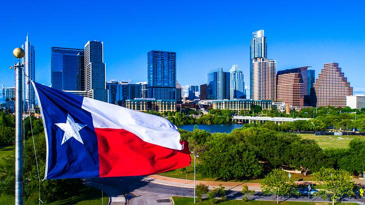 A red and white flag with one star on a pole, in front of a city skyline and park