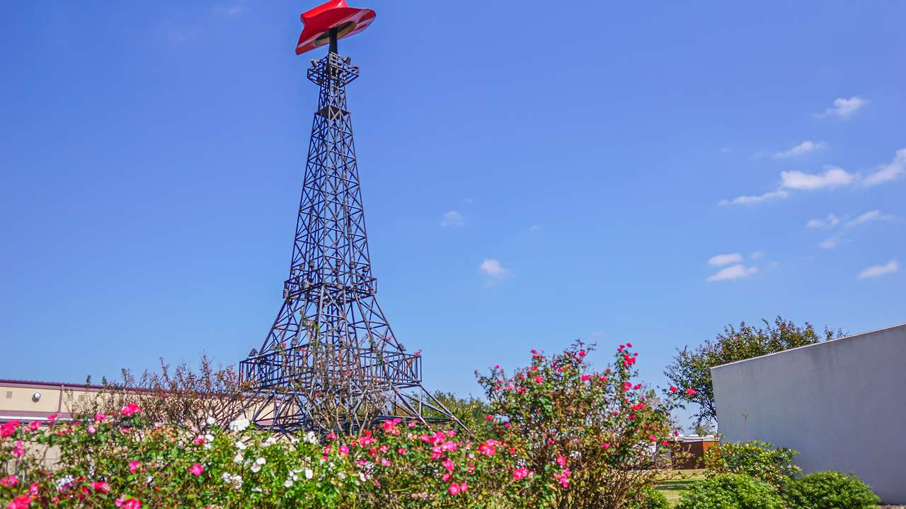 A tall metal "Eiffel Tower" replica with a red cowboy hat on top and flowers in front