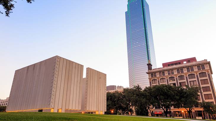 A tall glass building surrounded by smaller buildings and trees