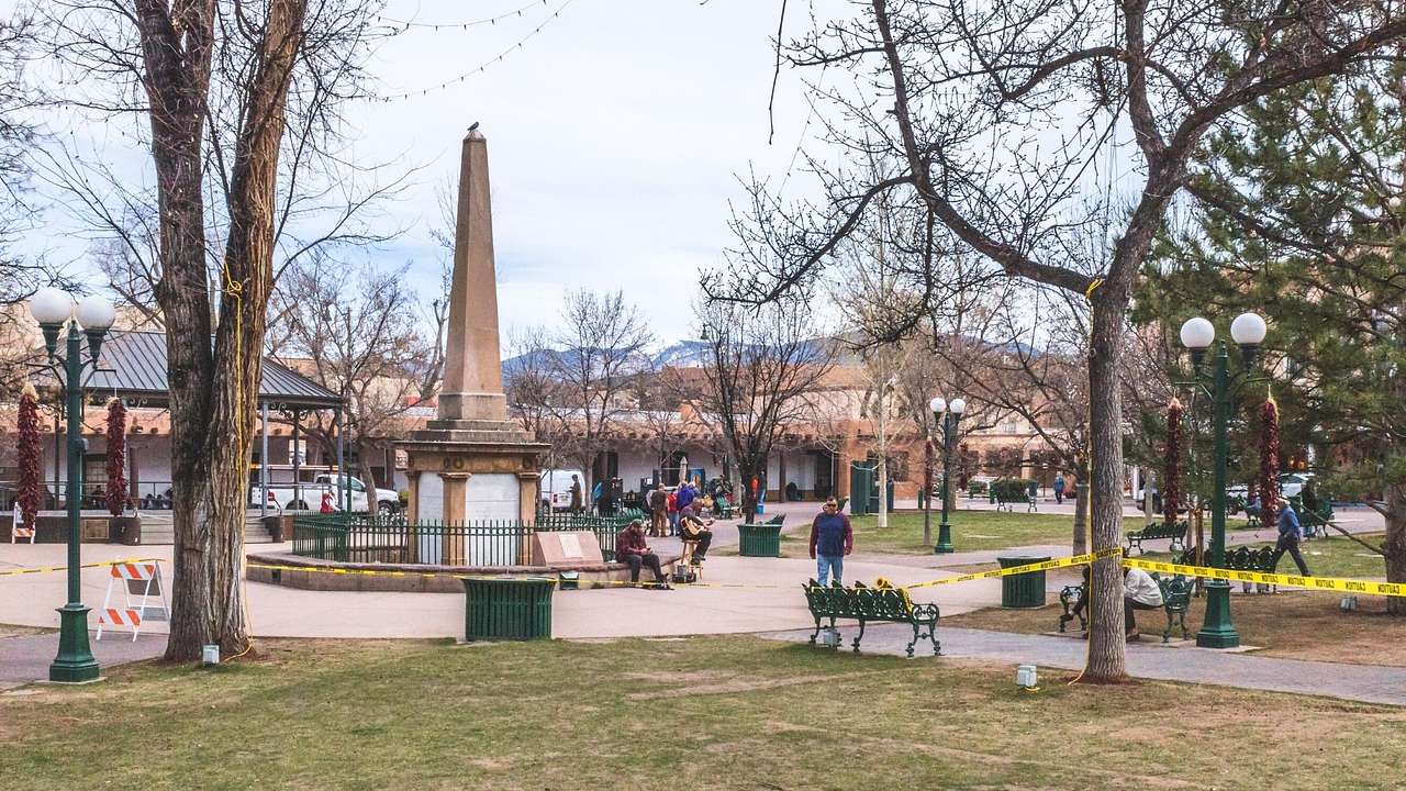 Local people hanging out on a square with a tall monument, trees, grass, and benches