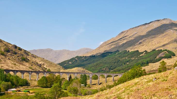A multi-arched train bridge from afar in between rolling hills on a clear day A multi-arched train bridge from afar in between rolling hills on a clear day