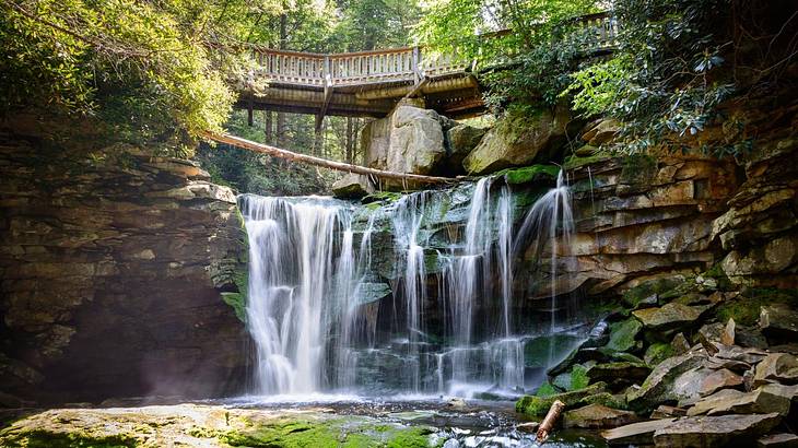 A waterfall cascading into a rocky pool with trees and a wooden bridge above