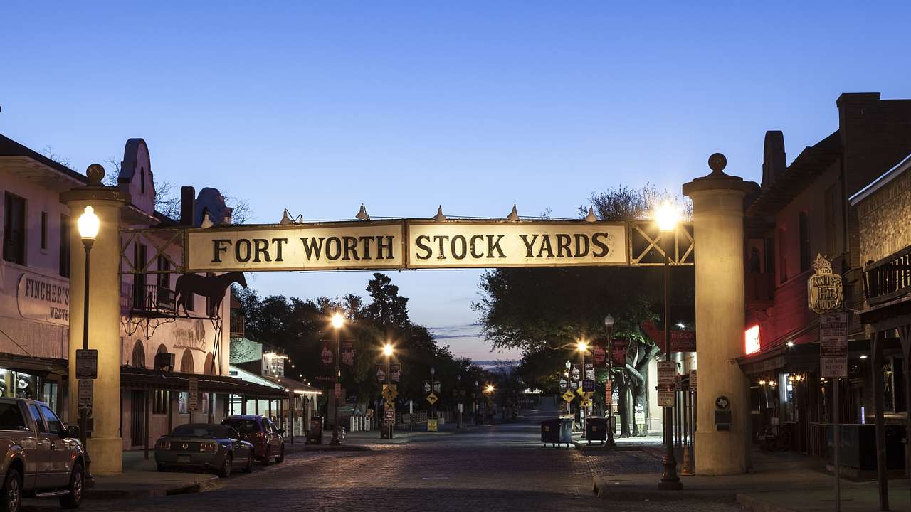 A sign across a road that says "Fort Worth Stock Yards" at night with street lights