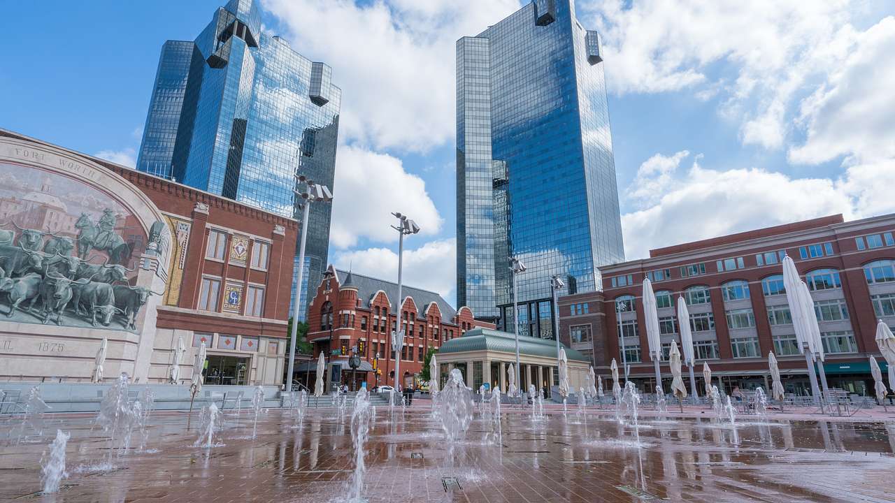 Outdoor water fountains near brick buildings and mirrored skyscrapers