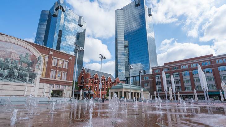 Outdoor water fountains near brick buildings and mirrored skyscrapers
