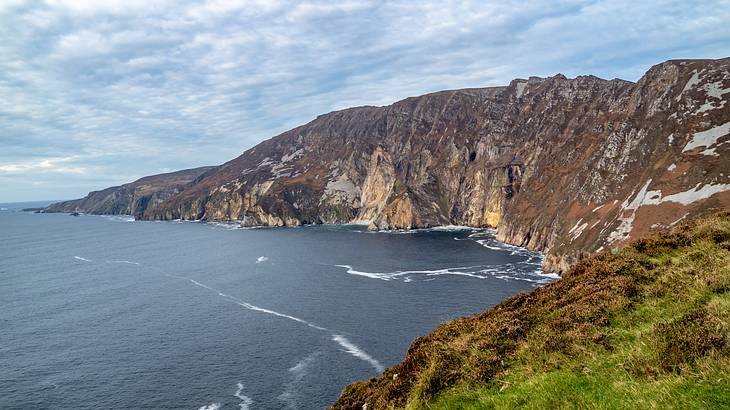 Rocky cliffs of a mountain by an ocean, under a cloudy sky