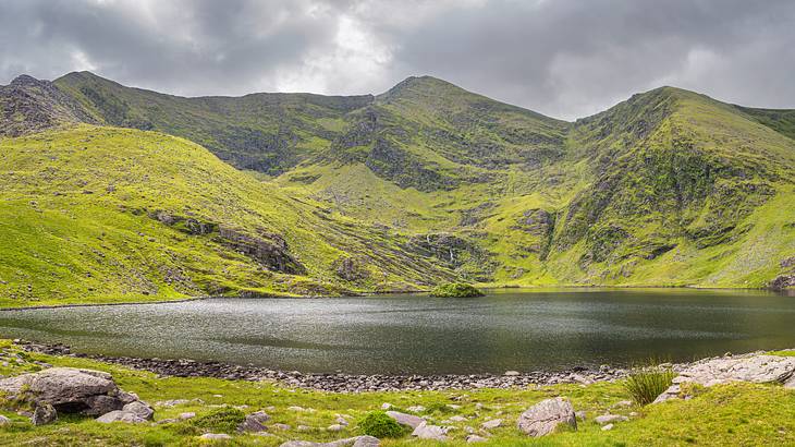 A lake at the base of a green mountain range on a cloudy day