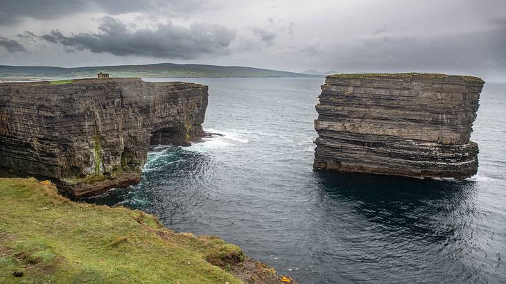 A cloudy sky in the background of multi-layered rock formations with water around