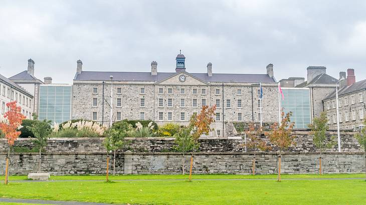 Flagpoles and a grassy lawn in front of a grey building with a clock