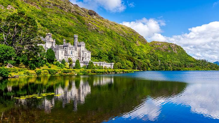 An abbey at the foot of a green mountain reflected in a lake