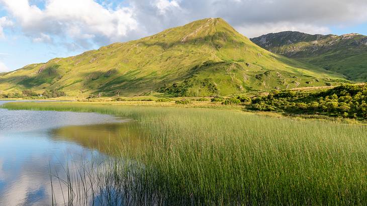 A lake at the foot of a green mountain under a partly cloudy sky