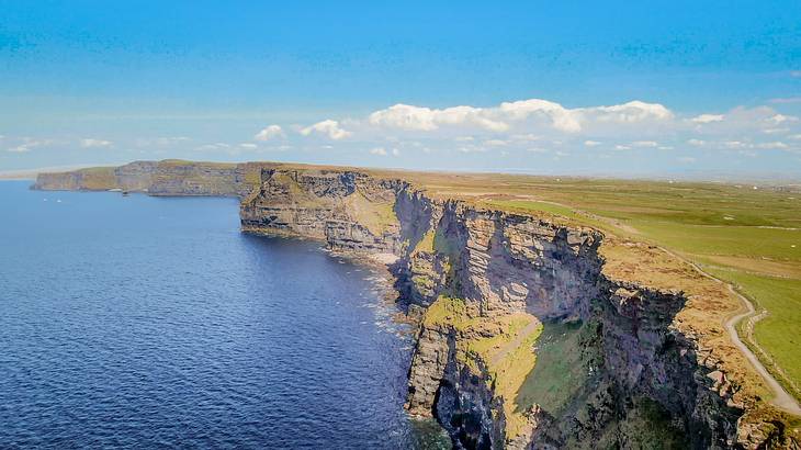 Aerial of a partly cloudy sky over green rocky cliffs and ocean