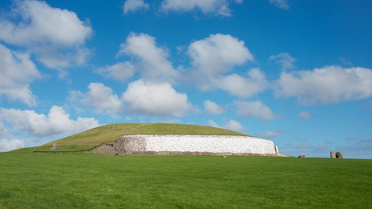 A passage of tombs on a green hill against a partly cloudy sky